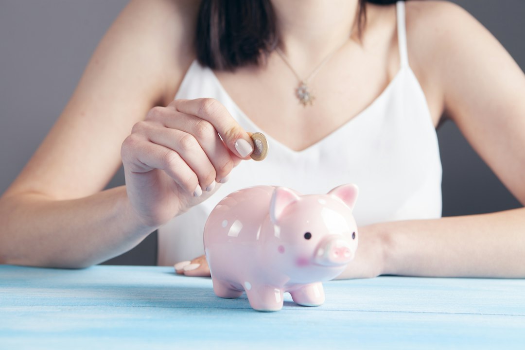 A close-up of a person's hand dropping a coin into a house-shaped piggy bank, symbolizing the concept of saving money on home selling commissions.
